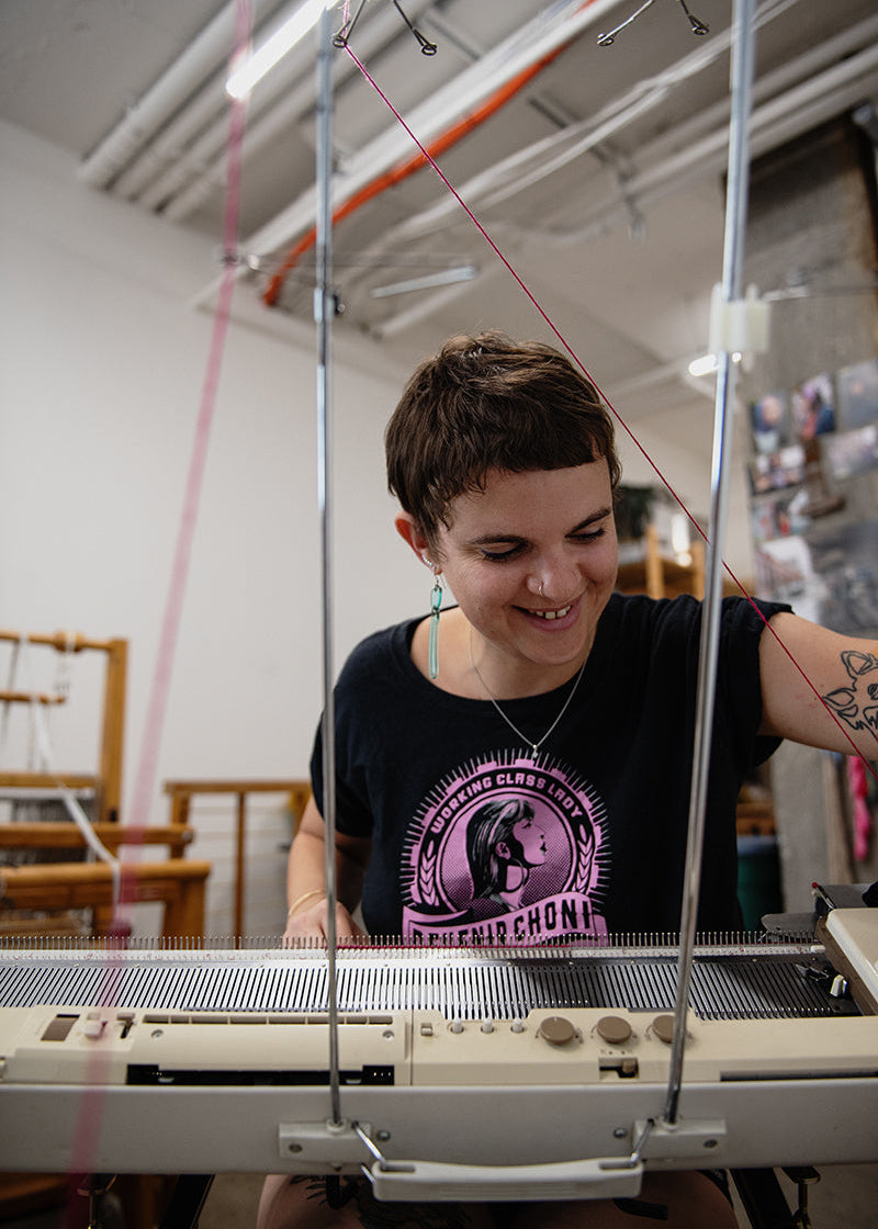 portrait de l'artiste Agathe Dessaux en train de tricoter sur sa machine à tricoter. 